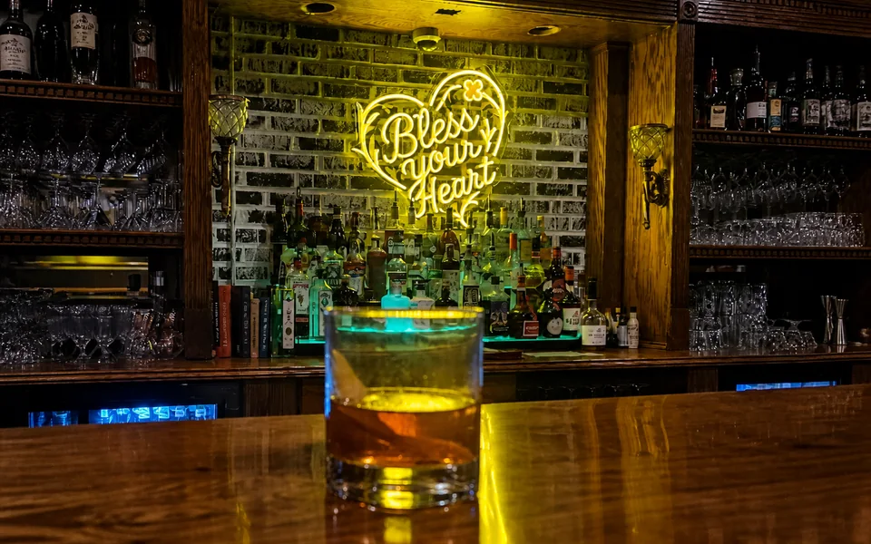 A house cocktail set before the illuminated Bless Your Heart bar